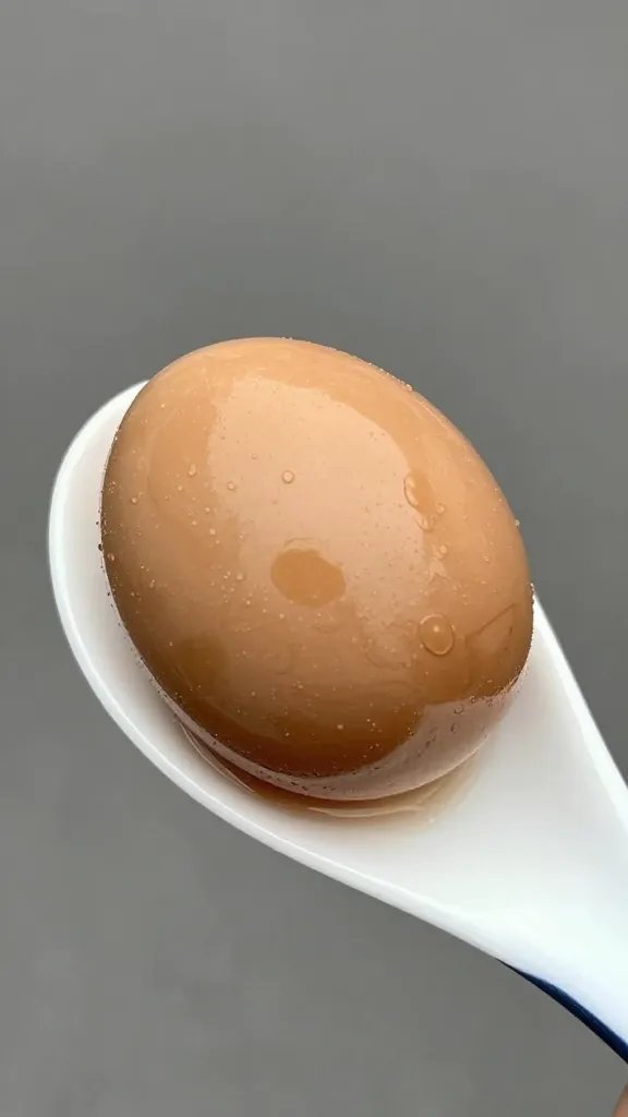 single soy-braised egg, bronze sheen, on white spoon