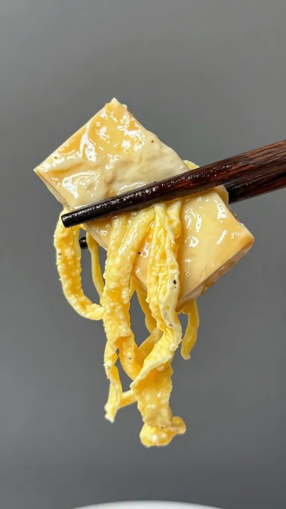 chopsticks holding saucy tofu with egg strands